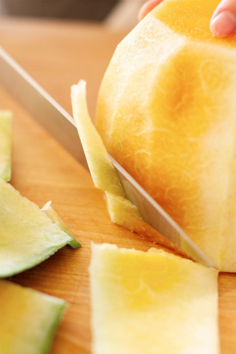 close up of knife shaving the rind off of a halved orange colored watermelon