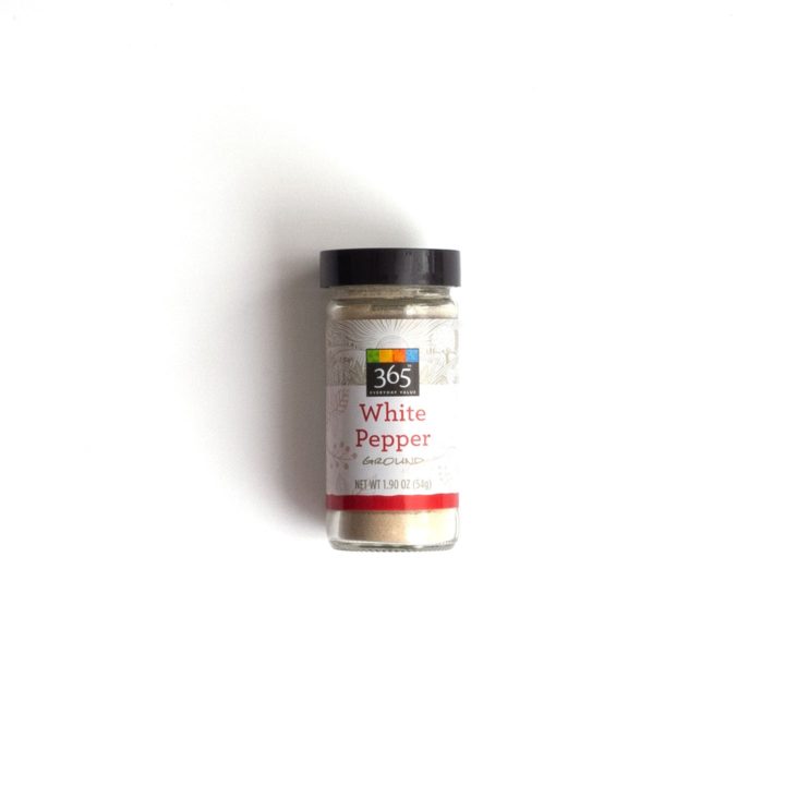 A small glass ground white pepper spice jar over a white background.