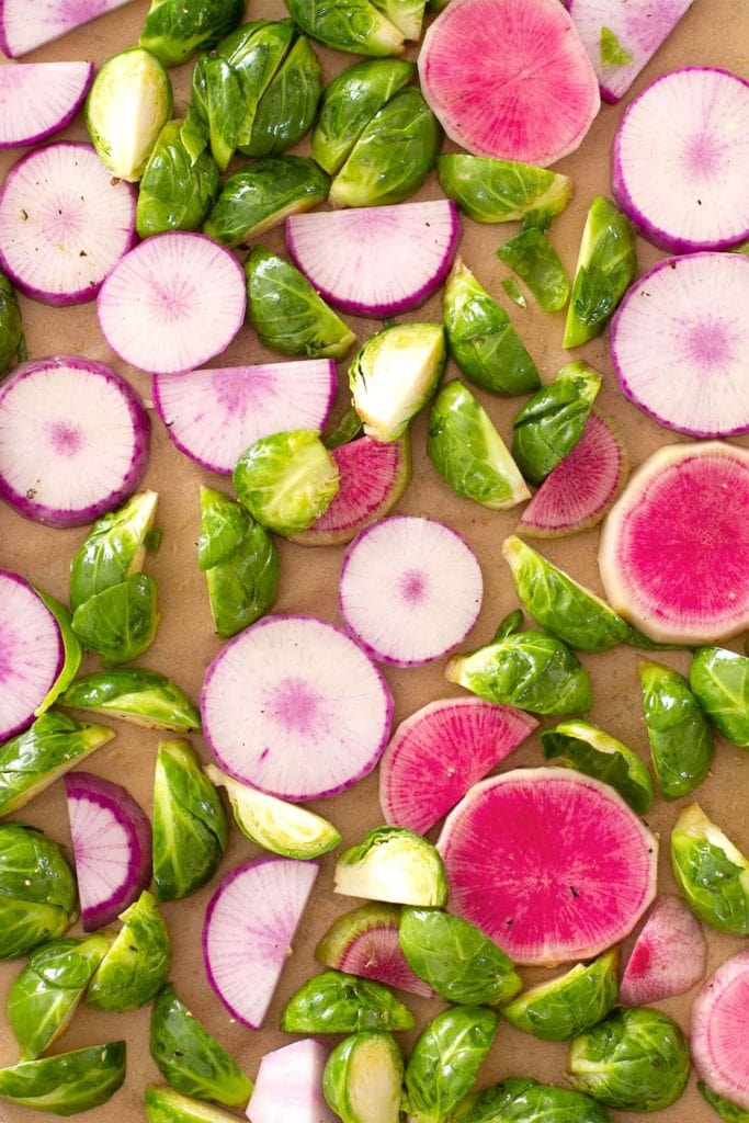Top down view of cut brussels sprouts and radish slices on a half sheet tray.