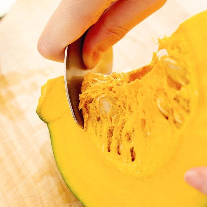 process shot of scooping seeds out of kabocha squash with a metal spoon