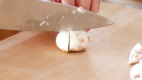 Sliced white button mushroom on a wood cutting board.