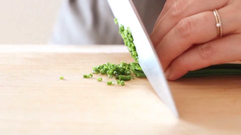 Fresh chives being minced on a wood cutting board.