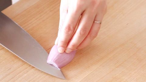 A person making horizontal slices on a peeled shallot.