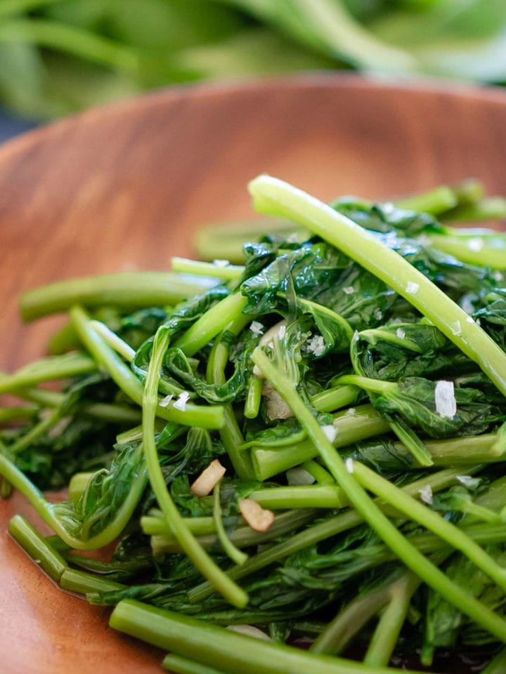A close up view of the cooked water spinach on a wood plate.