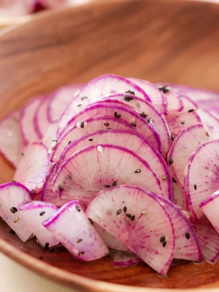 Thinly sliced purple daikon radish dressed with sesame oil, minced garlic, and toasted sesame seeds on a wood plate
