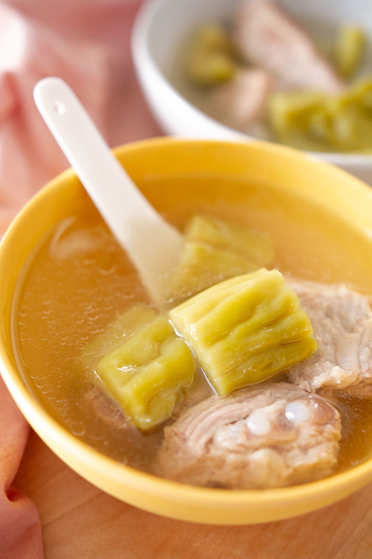 Bitter melon and pork rib soup in a yellow soup bowl with a white Chinese soup spoon.